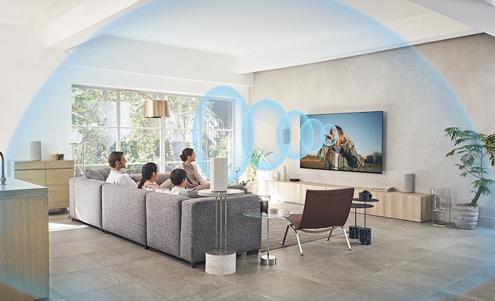 Family on a sofa watching TV with the HT-A9 Home Theatre System on a wooden cabinet with sound waves emanating from the screen.