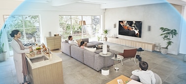 Family in room watching music concert on TV with the HT-A9 Home Theatre System on a wooden cabinet with a dome of sound waves