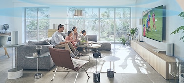 Family on a sofa watching TV with the HT-A9 Home Theatre System on a wooden cabinet and Immersive AE on and a dome of sound waves in the room.