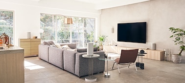 Living room setting showing the HT-A9 Home Theatre System on a wooden cabinet with speakers positioned on cabinet and around sofa