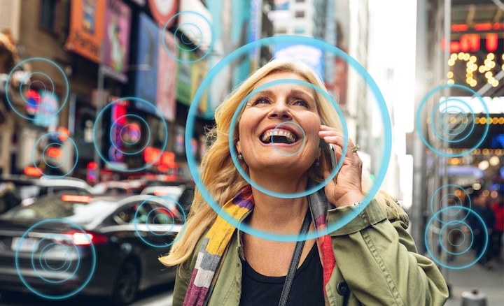 Woman in busy street scene talking on mobile phone, showing how Voice Zoom 2 makes speech easier to hear