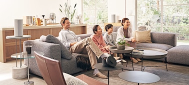 Family on a sofa watching TV with speakers around room creating an immersive experience