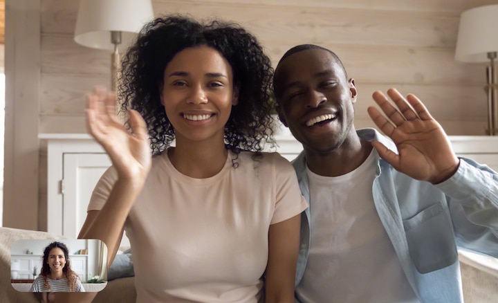 Image of couple in living room waving at a friend during video chat